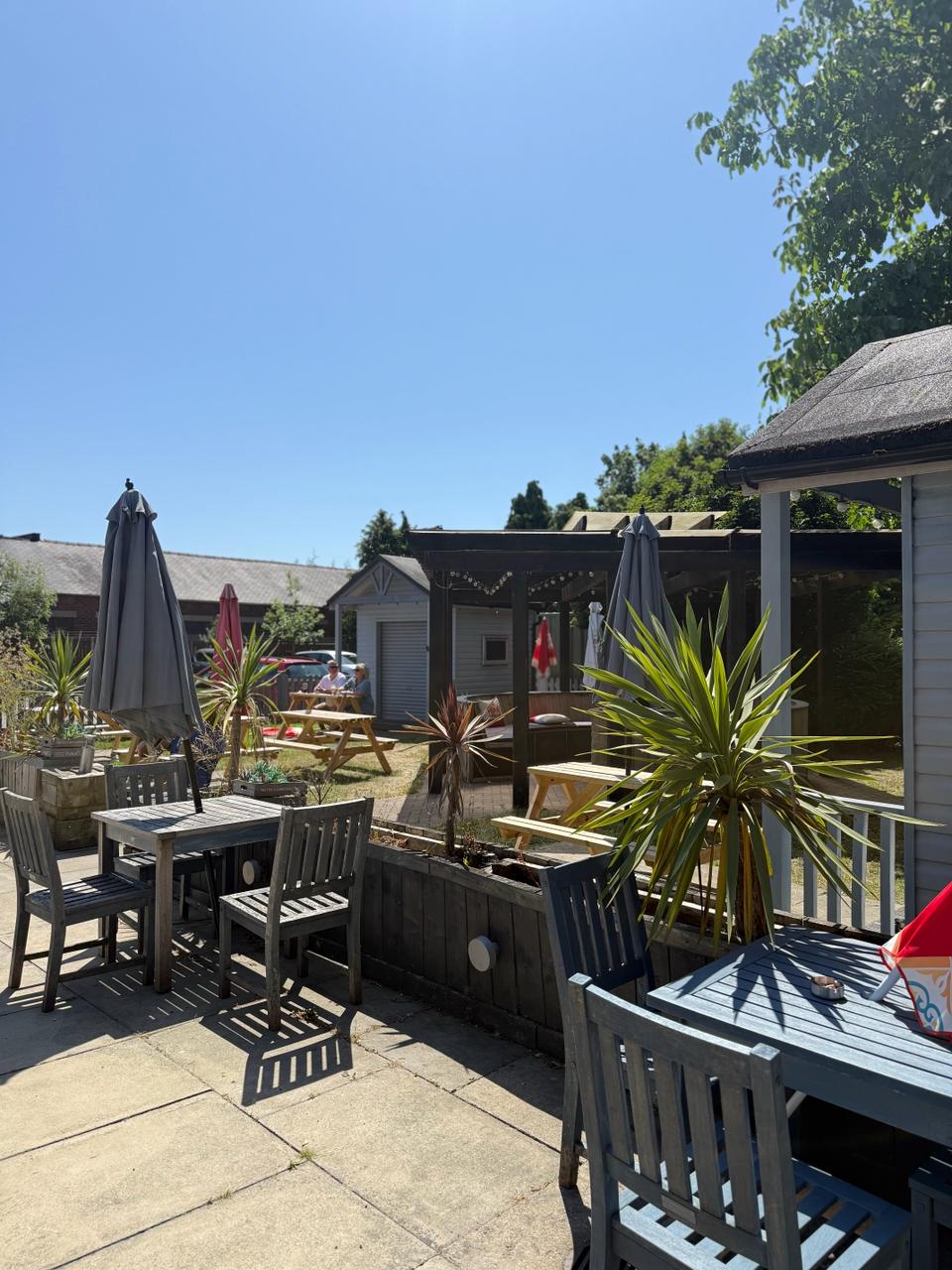 Sunny beer garden patio with wooden tables, parasols and palms